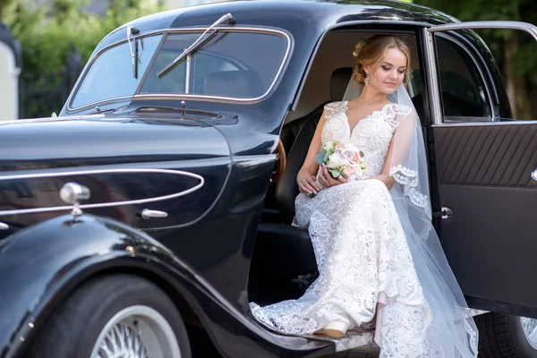 Beauty bride in bridal gown with bouquet and lace veil in the car — Stock Photo, Image