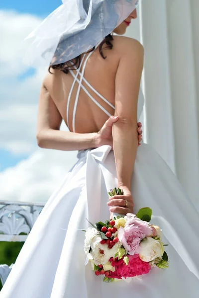 Невеста в свадебном платье с букетом и кружевной вуалью на природе — стоковое фото