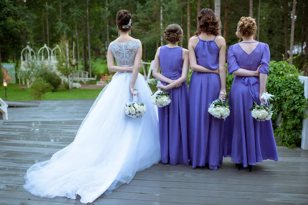 Beautiful bridesmaids and bride in bridal gown with bouquets in the nature