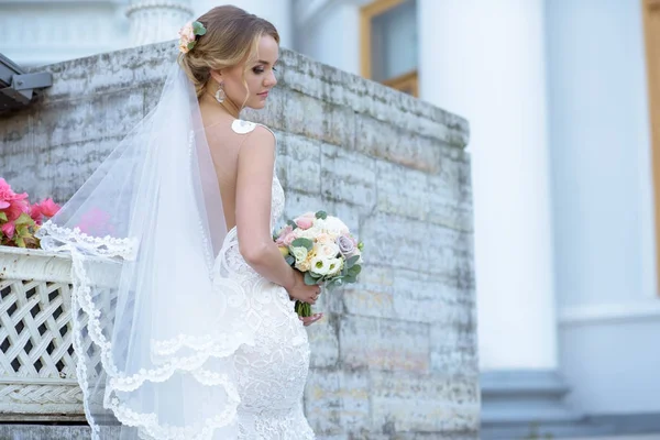 Невеста в свадебном платье с букетом и кружевной вуалью на природе — стоковое фото