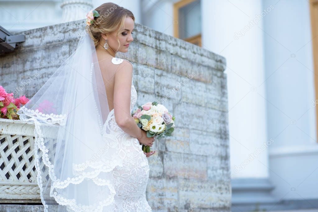 Beauty bride in bridal gown with bouquet and lace veil in the nature