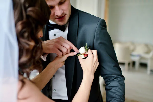 Brudgummen och bruden bär en boutonniere inomhus — Stockfoto