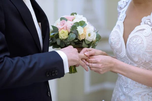 Noiva de beleza e noivo bonito estão usando anéis uns aos outros — Fotografia de Stock