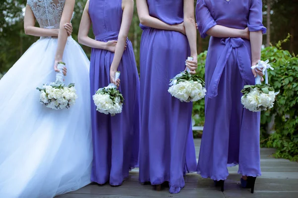 Hermosas damas de honor y novia en vestido de novia con ramos de flores en la naturaleza — Foto de Stock