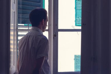 Adam karanlık bir odadan dışarı bakıyor. 