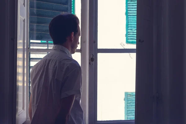 Mannen tittar ut genom fönstret från ett mörkt rum — Stockfoto