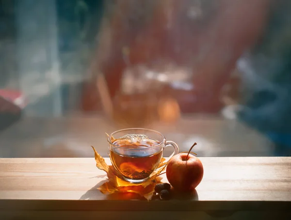 Outono Natureza morta: Chá em folhas de bordo em uma mesa de madeira perto da janela. Os raios do sol numa chávena de chá. Xícara de chá quente em um dia ensolarado em um fundo de janela . — Fotografia de Stock