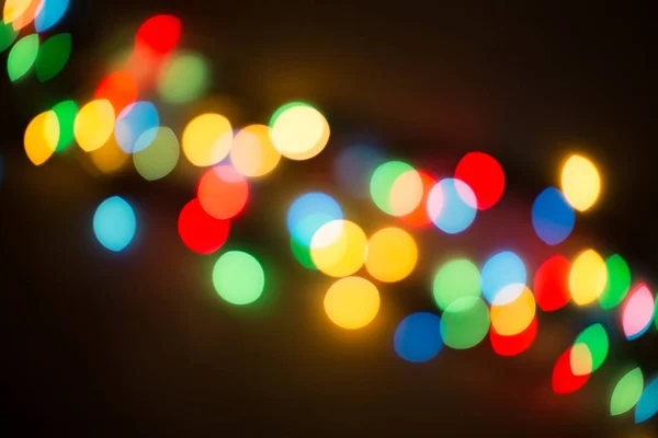 Bokeh lights. Color light on black background. Christmas or other holiday decorations, garland illumination bokeh. Abstract circular light bokeh New Year Festive background, decorated tree bokeh.