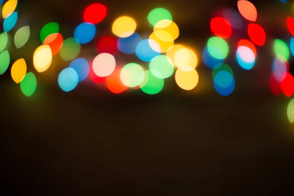 Bokeh lights. Color light on black background. Christmas or other holiday decorations, garland illumination bokeh. Abstract circular light bokeh New Year Festive background, decorated tree bokeh.