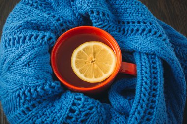 Cup of hot tea with lemon dressed in knitted warm winter scarf, warm knitted sweater or blanket. still life of a scarf and Cup of tea with lemon. Winter time. Cozy and soft winter background. clipart