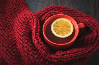 Cup of hot tea with lemon dressed in knitted warm winter scarf, warm knitted sweater or blanket. still life of a scarf and Cup of tea with lemon. Winter time. Cozy and soft winter background. clipart