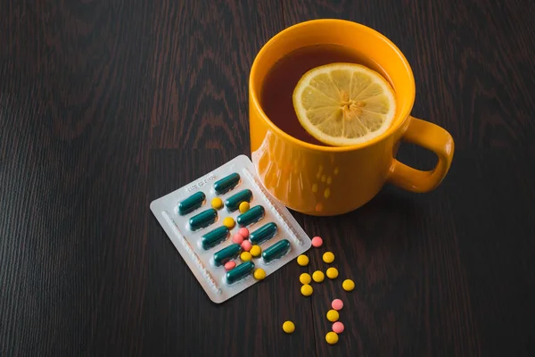 healthcare, traditional medicine and flu concept - tea cup with lemon and pills. Medical pills and hot tea with lemon, treatment of colds, flu and runny.