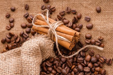 Kahve çekirdekleri ve tarçın çuval bezi bir arka plan üzerinde. Kavrulmuş kahve çekirdekleri arka plan kapatın. Üst metin kopyalama yeri olan kahve çekirdekleri kazık. Baharat. Baharat. Tarçın. Badian. Kahve evi.