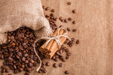 Kahve çekirdekleri ve tarçın çuval bezi bir arka plan üzerinde. Kavrulmuş kahve çekirdekleri arka plan kapatın. Üst metin kopyalama yeri olan kahve çekirdekleri kazık. Baharat. Baharat. Tarçın. Badian. Kahve evi.