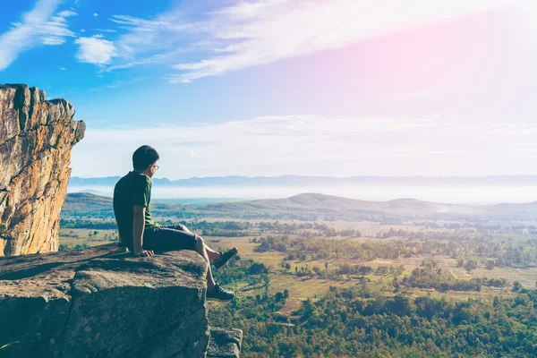 Young man in green sportswear is sitting on cliff's edge — Stock Photo, Image