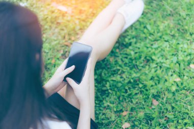 Güzel genç Asyalı kadın bahçede Smartphone kullanarak