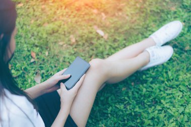 Güzel genç Asyalı kadın bahçede Smartphone kullanarak