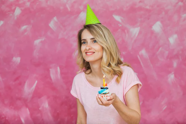 Vacker blond flicka i födelsedag cap håller cupcake med ljus — Stockfoto