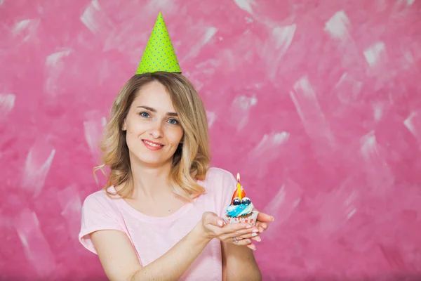 Güzel sarışın kız doğum günü şapkalı cupcake mum ile tutun — Stok fotoğraf