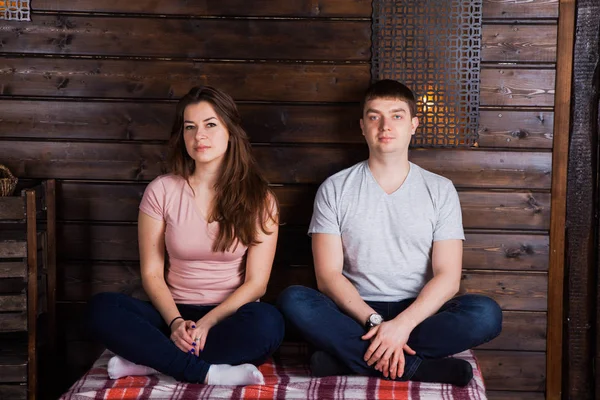 Молодая пара сидит крестиком на клетчатой возле темной деревянной стены. C — стоковое фото