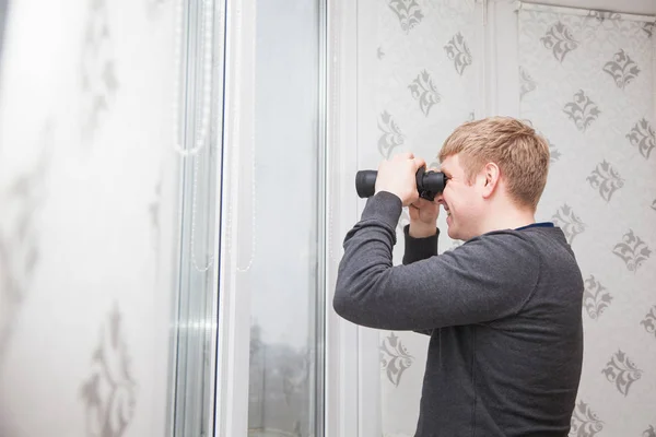 Young handsome man looking through window with binocular glasses — Stock Photo, Image