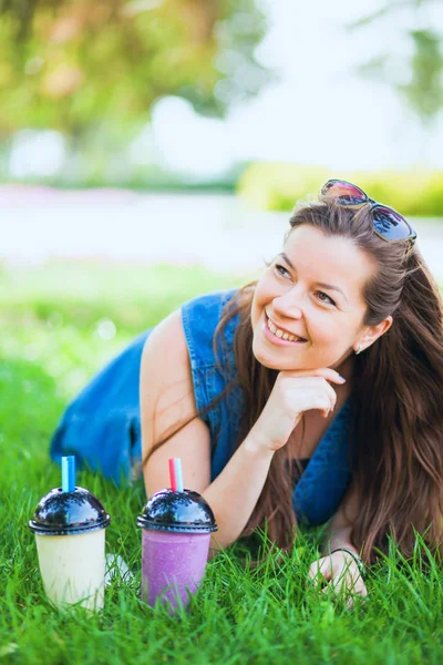 Bununla birlikte güneş gözlüklü genç kadın iç sulu lezzetli milkshakes yeşil çim çimen