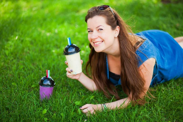 Pretty young woman drink smoothie on green grass