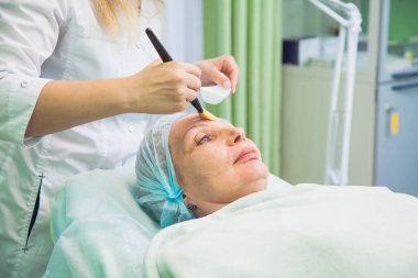 Güzellik uzmanı kadın kıdemli yüzünde maske uygulanıyor. Cilt Gençleştirme kavramı.