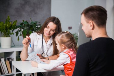 Genç profesyonel çocuk doktoru reçete için bir alt gösterir. Babası onun Kliniği ofisinde küçük bir kız için çocuk doktor göstermek danışmanlık