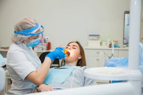 Female dentist work with light-curing seal, patient with caries on chair.