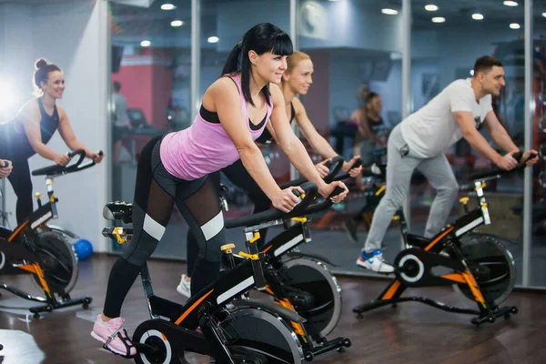 Spor salonunda bisiklet dersi, kardiyo makinesinde dönen bir grup formda insan.