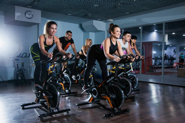 Spor salonunda bisiklet dersi, kardiyo makinesinde dönen bir grup formda insan.