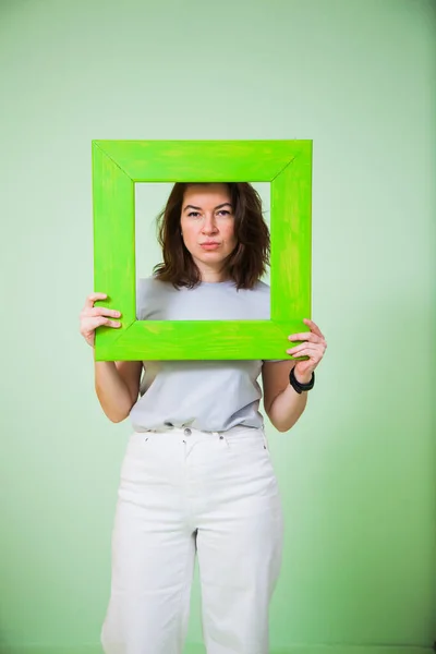 Young woman with green wooden frame on light background. — Stock Photo, Image