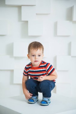 Küçük çocuk stüdyoda beyaz küpün üzerinde oturuyor..