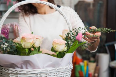 Çiçekçi kadın tasarımcı çiçek topluyor ve beyaz sepetten buket yapıyor.