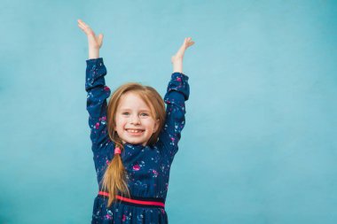 Kot ceketli mutlu kız elleri havada gülümsüyor.