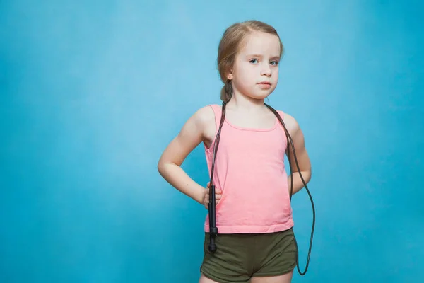 Pretty little sporty girl with skipping rope on blue background.