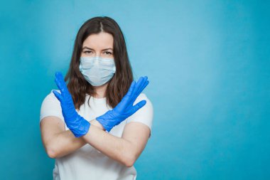 Antiviral tıbbi maskeli ve koruyucu eldivenli genç bir kadın dur işareti gösteriyor..