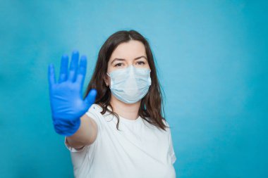Antiviral tıbbi maskeli ve koruyucu eldivenli genç bir kadın dur işareti gösteriyor..