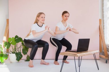 İki kız kardeş evde dizüstü bilgisayarlarıyla karantinada spor yapıyor..