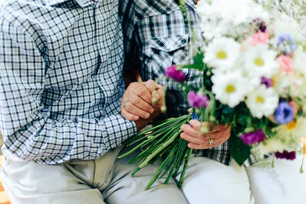 two old people are sitting on a bench and holding each other's hands against a beautiful bouquet of flowers