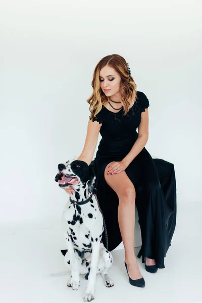 beautiful attractive girl in a black dress with a Dalmatian dog on white background