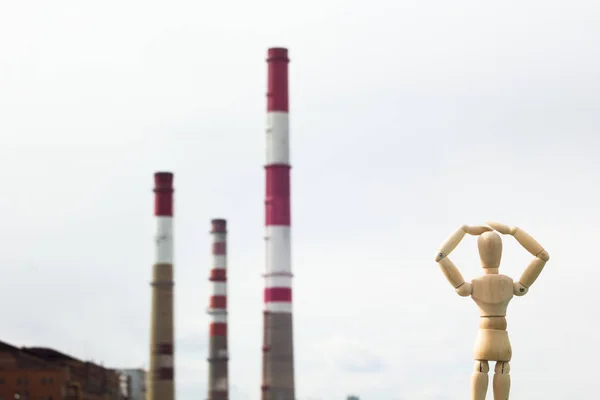 Wooden toy in the image of a man against the background of smoking pipes of a factory