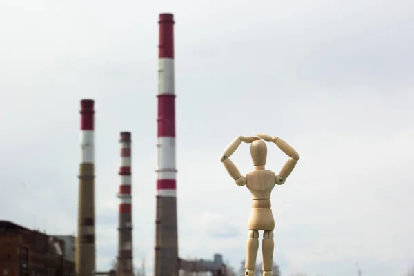 Wooden toy in the image of a man against the background of smoking pipes of a factory