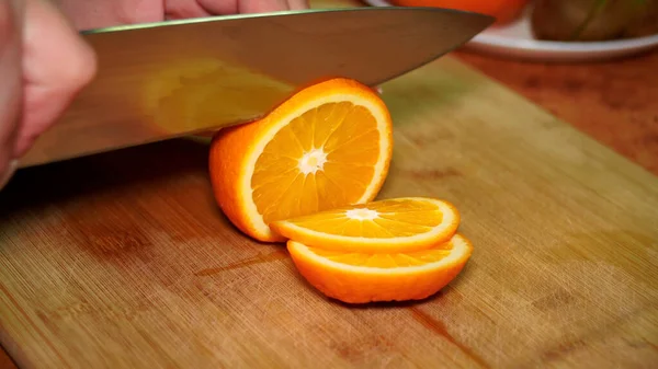 girl on a wooden board cuts with a knife a ripe juicy vitamin orange