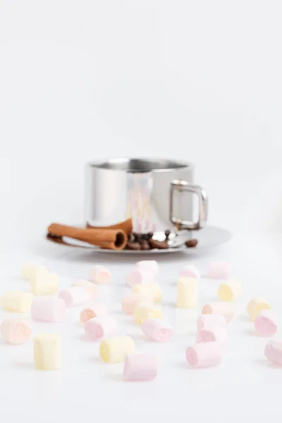 Marshmallows multicoloridos em um fundo branco. Atrás deles está uma xícara de café com grãos e canela . — Fotografia de Stock