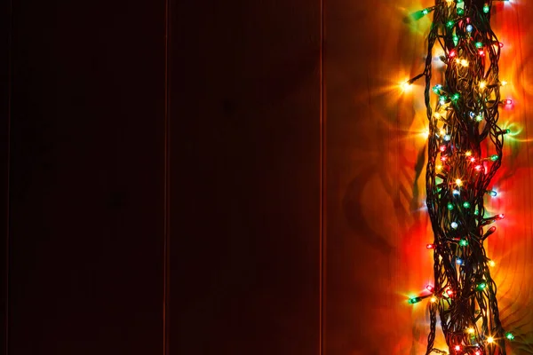 Glowing Christmas garland on the wooden background in the darkness.