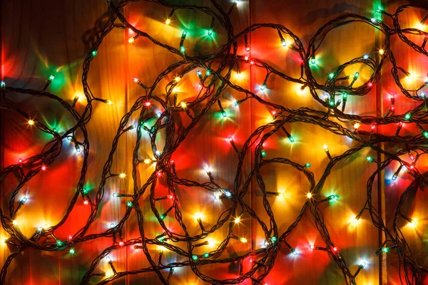 Glowing Christmas garland on the wooden background in the darkness. — Stock Photo, Image