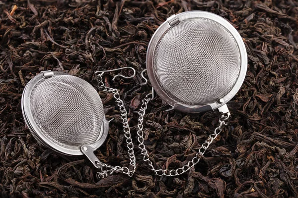 Two tea filter on a chain with black tea on a pile of dry tea leaves. A tea filter is a close-up of a kitchen accessory.