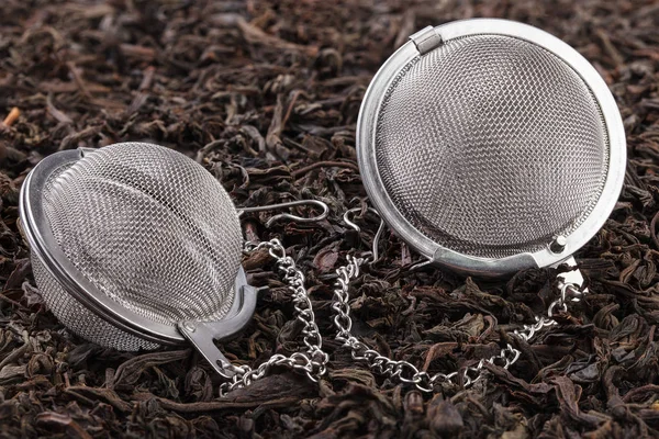 Two tea filter on a chain with black tea on a pile of dry tea leaves. A tea filter is a close-up of a kitchen accessory.